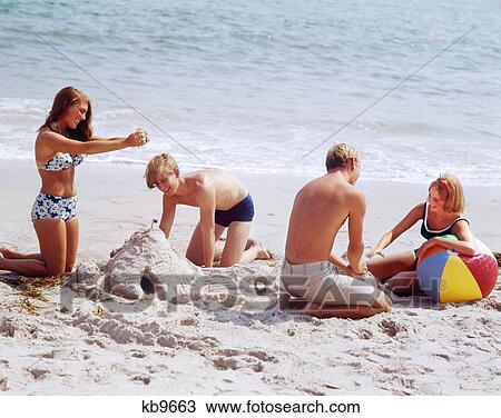 1960S 1970S Two Teenage Couples On Beach Building Sandcastle And Playing With Ball View Large Photo Image Stock Image - 1960S 1970S Two Teenage Couples On Beach Building Sandcastle And Playing With Ball. Fotosearch
