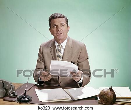 1960s BUSINESSMAN SITTING AT DESK LOOK AT CAMERA HOLDING PAPERS View Large Photo Image Stock Image - 1960s BUSINESSMAN SITTING AT DESK LOOK AT CAMERA HOLDING PAPERS. Fotosearch
