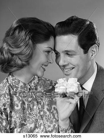 Stock Photography - 1960s COUPLE SMILING HOLDING A PAIR OF BABY BOOTIES. Fotosearch