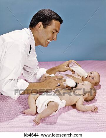 Picture - 1960S Father Feeding Twin Babies With Bottles Simultaneously. Fotosearch