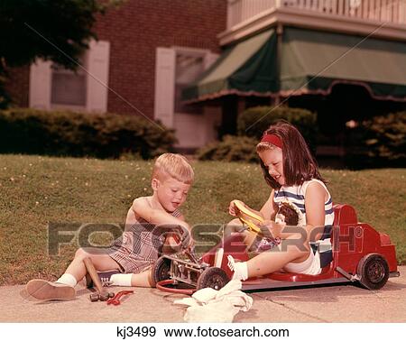 1960s GIRL SITTING IN RED TOY CAR ON SIDEWALK BOY PLAYING MECHANIC TRYING TO FIX FRONT WHEELS View Large Photo Image Stock Photo - 1960s GIRL SITTING IN RED TOY CAR ON SIDEWALK BOY PLAYING MECHANIC TRYING TO FIX FRONT WHEELS. Fotosearch