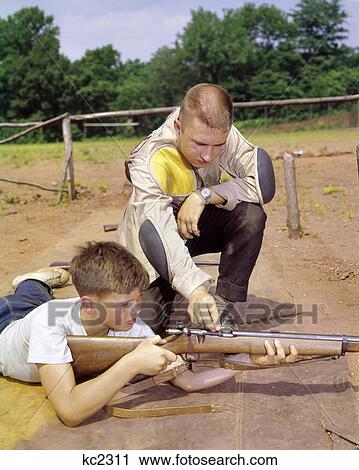 1960s MAN FATHER COACHING TEACHING TEEN BOY SON GUN SAFETY ON RIFLE FIRING RANGE View Large Photo Image Stock Image - 1960s MAN FATHER COACHING TEACHING TEEN BOY SON GUN SAFETY ON RIFLE FIRING RANGE. Fotosearch
