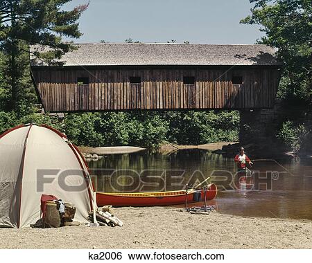 1960s MAN STANDING IN STREAM FLY FISHING BESIDE CAMPSITE TENT CANOE ON RIVERBANK COVERED BRIDGE BACKGROUND View Large Photo Image Stock Photograph - 1960s MAN STANDING IN STREAM FLY FISHING BESIDE CAMPSITE TENT CANOE ON RIVERBANK COVERED BRIDGE BACKGROUND. Fotosearch