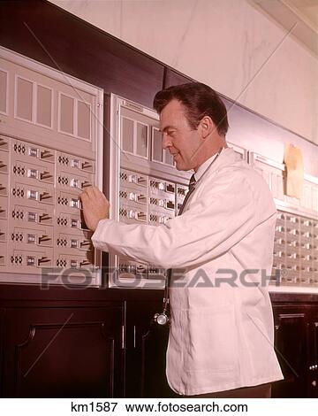Stock Photo - 1960s MEDICAL DOCTOR RETRIEVING SUPPLIES FROM SECURE STORAGE. Fotosearch