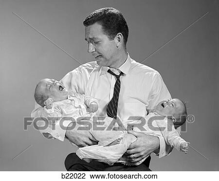 Stock Image - 1960s PANICKED MAN FATHER HOLDING CRYING TWIN BABIES. Fotosearch