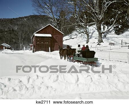 Stock Image - 1960s PEOPLE RIDING IN HORSE DRAWN WINTER SLEIGH IN SNOWY RURAL VERMONT USA. Fotosearch