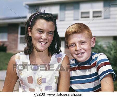 Stock Image - 1960S Portrait Smiling Boy And Girl Brother And Sister Together Looking At Camera In Front Of Suburban House. Fotosearch