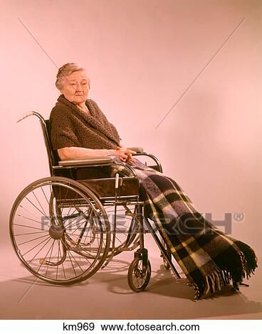 1960s SENIOR WOMAN SITTING IN A WHEELCHAIR LOOKING AT CAMERA WITH SERIOUS EXPRESSION WEARING PLAID LAP ROBE AND WOOL KNIT SHAWL View Large Photo Image Stock Photo - 1960s SENIOR WOMAN SITTING IN A WHEELCHAIR LOOKING AT CAMERA WITH SERIOUS EXPRESSION WEARING PLAID LAP ROBE AND WOOL KNIT SHAWL. Fotosearch