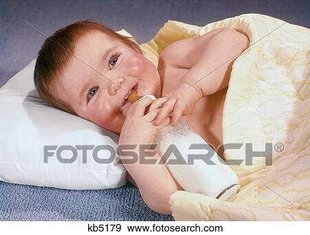 1960s SMILING BABY WRAPPED IN BLANKET LYING ON PILLOW HOLDING MILK BOTTLE View Large Photo Image Stock Photo - 1960s SMILING BABY WRAPPED IN BLANKET LYING ON PILLOW HOLDING MILK BOTTLE. Fotosearch