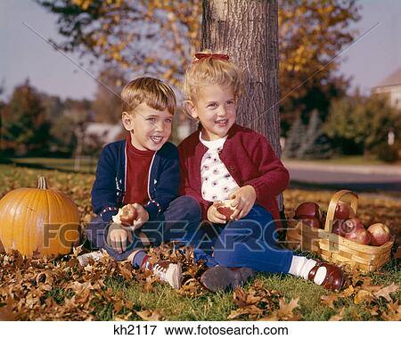1960s SMILING BOY AND GIRL EATING APPLES SITTING UNDER AUTUMN TREE WITH PUMPKIN AND BASKET OF APPLES View Large Photo Image Stock Photo - 1960s SMILING BOY AND GIRL EATING APPLES SITTING UNDER AUTUMN TREE WITH PUMPKIN AND BASKET OF APPLES. Fotosearch