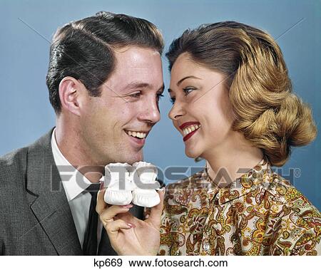 Stock Photo - 1960s SMILING COUPLE HEADS TOGETHER OVER PAIR BABY BOOTIES. Fotosearch