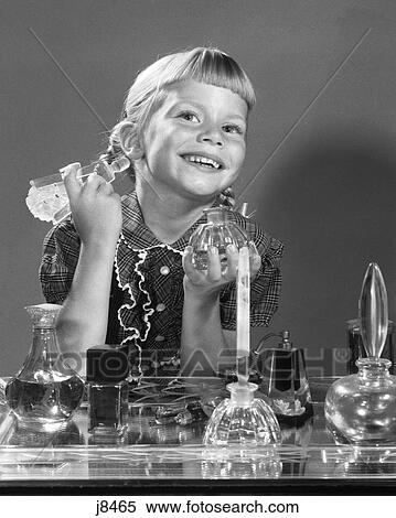 Stock Photography - 1960S Smiling Little Girl Sitting At MotherS Bureau Vanity Perfume Bottles In Front Looking At Camera In Mirror. Fotosearch