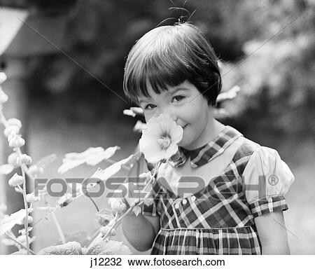 Stock Image - 1960S Smiling Little Girl Smelling Flower. Fotosearch
