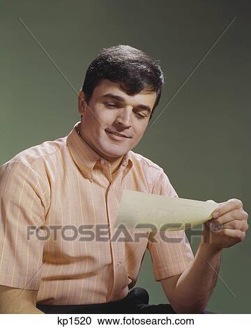 Stock Image - 1960s SMILING MAN LOOKING AT CHECK. Fotosearch