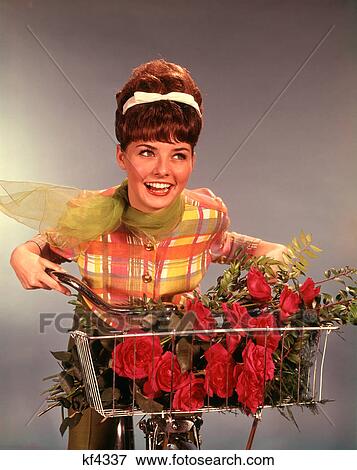 1960s SMILING TEEN GIRL WITH TEASED BRUNETTE BOUFFANT HAIRDO RIDING BICYCLE WITH RED ROSES BOUQUET IN BASKET View Large Photo Image Stock Photo - 1960s SMILING TEEN GIRL WITH TEASED BRUNETTE BOUFFANT HAIRDO RIDING BICYCLE WITH RED ROSES BOUQUET IN BASKET. Fotosearch