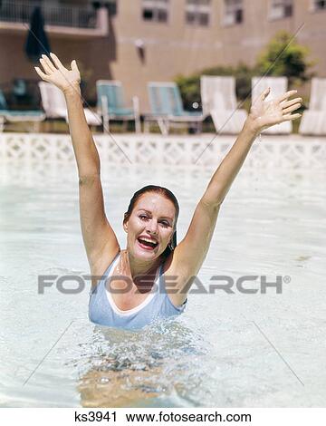 1960s SMILING WOMAN BLUE BATHING SUIT JUMPING OUT OF SWIMMING POOL WATER ARMS RAISED OVER HER HEAD LOOKING AT CAMERA View Large Photo Image Stock Image - 1960s SMILING WOMAN BLUE BATHING SUIT JUMPING OUT OF SWIMMING POOL WATER ARMS RAISED OVER HER HEAD LOOKING AT CAMERA. Fotosearch
