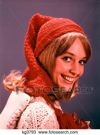 Stock Image - 1960s SMILING YOUNG WOMAN WITH ICE SKATES WOOL HAT AND SWEATER LOOKING AT CAMERA. Fotosearch