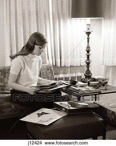 Picture - 1960s TEENAGE GIRL SITTING ON COUCH AT HOME SORTING VINYL RECORD ALBUMS. Fotosearch
