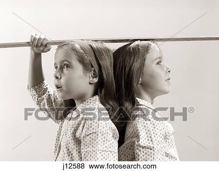 1960s TWINS GIRLS STANDING BACK TO BACK UNDER YARD STICK MEASURING HEIGHT View Large Photo Image Stock Photo - 1960s TWINS GIRLS STANDING BACK TO BACK UNDER YARD STICK MEASURING HEIGHT. Fotosearch