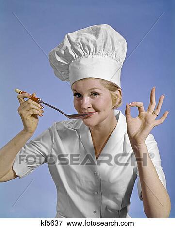 Stock Photo - 1960S WOMAN CHEF WEARING TOQUE LOOKING AT CAMERA TASTING FOOD MAKING OKAY SIGN SMILING. Fotosearch