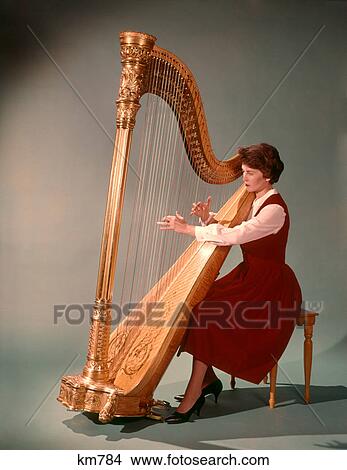 Picture - 1960s WOMAN PLAYING LARGE GOLDEN CONCERT OR PEDAL CHROMATIC HARP. Fotosearch