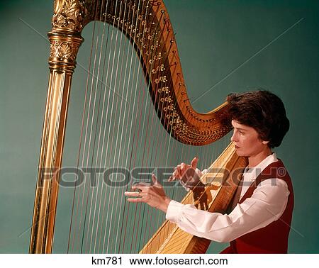 Stock Image - 1960s WOMAN PLAYING LARGE GOLDEN CONCERT OR PEDAL CHROMATIC HARP. Fotosearch