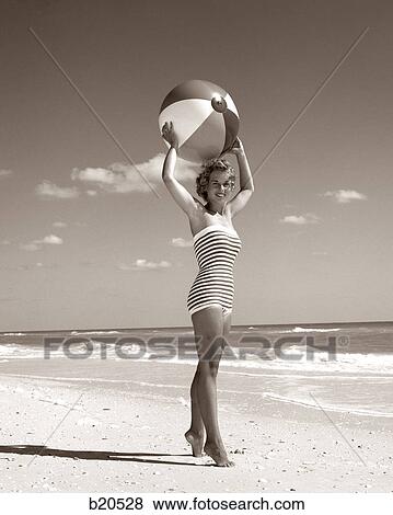 1960s YOUNG WOMAN STANDING ON TIPTOES WEARING STRAPLESS STRIPED BATHING SUIT HOLDING BEACH BALL OVER HEAD View Large Photo Image Stock Photo - 1960s YOUNG WOMAN STANDING ON TIPTOES WEARING STRAPLESS STRIPED BATHING SUIT HOLDING BEACH BALL OVER HEAD. Fotosearch