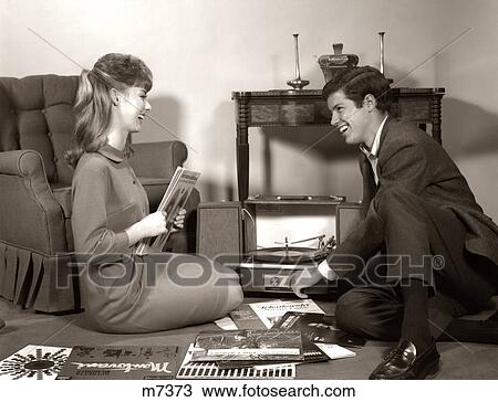 Stock Image - 1962s YOUNG COUPLE MAN WOMAN BROWSING LISTENING VINYL RECORDS. Fotosearch