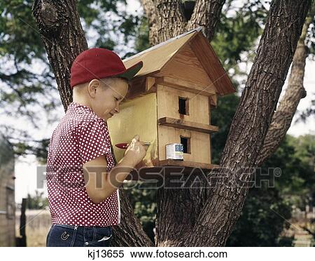 Stock Photography - 1970S 1980S Boy Painting Bird House Wearing Red Baseball Cap. Fotosearch