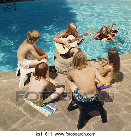 1970s 6 TEENS AROUND SWIMMING POOL LISTENING TO GIRL PLAYING GUITAR View Large Photo Image Stock Image - 1970s 6 TEENS AROUND SWIMMING POOL LISTENING TO GIRL PLAYING GUITAR. Fotosearch