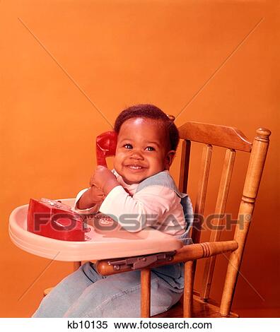 Stock Photography - 1970S African American Baby Babies Sitting High Chair Holding Red Toy Telephone. Fotosearch