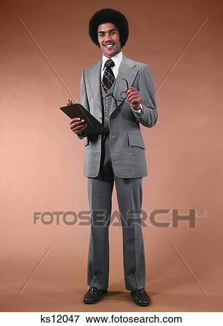 1970s AFRICAN AMERICAN MAN BUSINESSMAN SUIT HOLDING GLASSES CLIPBOARD SMILING LOOKING AT CAMERA View Large Photo Image Stock Photo - 1970s AFRICAN AMERICAN MAN BUSINESSMAN SUIT HOLDING GLASSES CLIPBOARD SMILING LOOKING AT CAMERA. Fotosearch