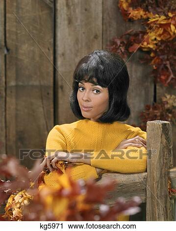 1970s AFRICAN AMERICAN YOUNG WOMAN GOLD SWEATER LEAN ON WOODEN FENCE AUTUMN LEAVES FASHION PORTRAIT LOOKING AT CAMERA View Large Photo Image Stock Image - 1970s AFRICAN AMERICAN YOUNG WOMAN GOLD SWEATER LEAN ON WOODEN FENCE AUTUMN LEAVES FASHION PORTRAIT LOOKING AT CAMERA. Fotosearch