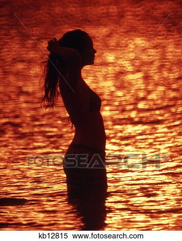 1970S Anonymous Silhouetted Woman Posing In Ocean Water Bathed In Sunset Light View Large Photo Image Stock Photography - 1970S Anonymous Silhouetted Woman Posing In Ocean Water Bathed In Sunset Light. Fotosearch