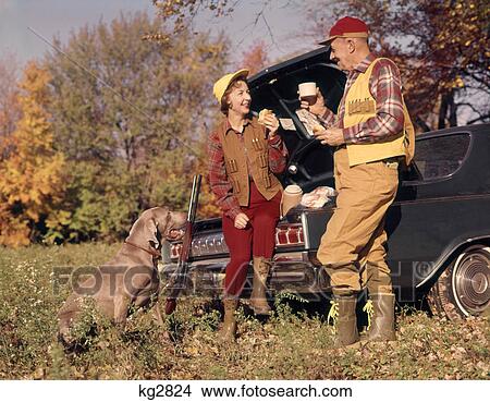 1970s ATTENTIVE WEIMARANER DOG WATCHING HUNTING COUPLE MAN AND WOMAN SITTING ON STANDING BY CAR TRUNK TALKING AND EATING LUNCH View Large Photo Image Picture - 1970s ATTENTIVE WEIMARANER DOG WATCHING HUNTING COUPLE MAN AND WOMAN SITTING ON STANDING BY CAR TRUNK TALKING AND EATING LUNCH. Fotosearch