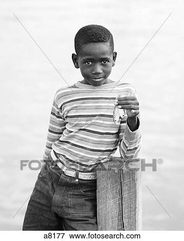 1970s BAHAMIAN BOY IN STRIPED SHIRT WITH SAD FACIAL EXPRESSION LOOKING AT CAMERA ON DOCK HOLDING UP TWO VERY SMALL FISH View Large Photo Image Stock Photo - 1970s BAHAMIAN BOY IN STRIPED SHIRT WITH SAD FACIAL EXPRESSION LOOKING AT CAMERA ON DOCK HOLDING UP TWO VERY SMALL FISH. Fotosearch