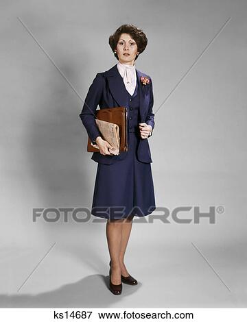 1970s BUSINESSWOMAN STANDING LOOKING AT CAMERA WITH SERIOUS FACIAL EXPRESSION HOLDING NEWSPAPER AND BRIEFCASE WEARING BLUE SUIT View Large Photo Image Stock Photo - 1970s BUSINESSWOMAN STANDING LOOKING AT CAMERA WITH SERIOUS FACIAL EXPRESSION HOLDING NEWSPAPER AND BRIEFCASE WEARING BLUE SUIT. Fotosearch
