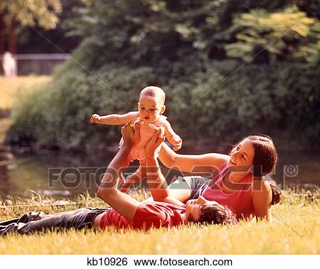 1970S Couple Lying In Grass Holding Baby Up Above Father View Large Photo Image Stock Photograph - 1970S Couple Lying In Grass Holding Baby Up Above Father. Fotosearch