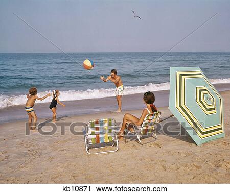 1970s FAMILY AT THE OCEAN BEACH BALL BATHING SUITS ALUMINUM CHAIRS UMBRELLA SAND SURF View Large Photo Image Stock Image - 1970s FAMILY AT THE OCEAN BEACH BALL BATHING SUITS ALUMINUM CHAIRS UMBRELLA SAND SURF. Fotosearch