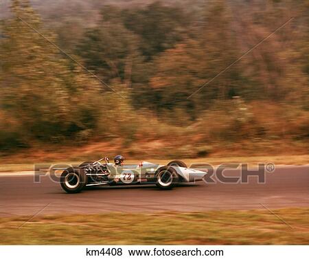 Stock Photo - 1970s GREEN RACE RACING CAR NUMBER 72 WITH DRIVER SPEEDING ALONG WOODED TRACK. Fotosearch