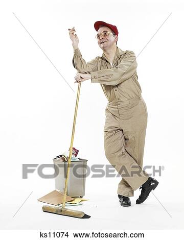1970s JANITOR MAINTENANCE MAN LEANING ON BROOM BY WASTEBASKET SMOKING CIGAR SMILING LOOKING UP WEARING RED CAP View Large Photo Image Picture - 1970s JANITOR MAINTENANCE MAN LEANING ON BROOM BY WASTEBASKET SMOKING CIGAR SMILING LOOKING UP WEARING RED CAP. Fotosearch