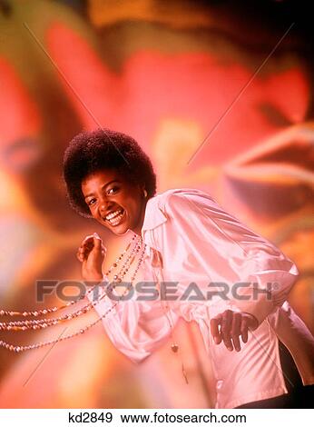 Stock Photo - 1970S Laughing Young African American Woman Afro Hair Style White Silk Shirt Singing Dancing Beads Swinging Looking At Camera. Fotosearch