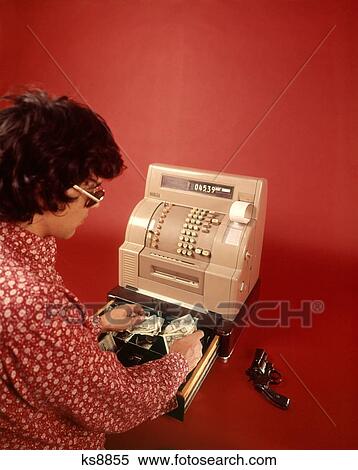 Stock Photography - 1970S Man Robber Armed With Gun Wearing Sunglasses Black Wig And Red Print Shirt Stealing Money From Cash Register Drawer. Fotosearch