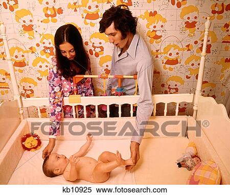 1970S Mother Father Couple Looking Touching Baby Lying In Nursery Crib View Large Photo Image Stock Photography - 1970S Mother Father Couple Looking Touching Baby Lying In Nursery Crib. Fotosearch