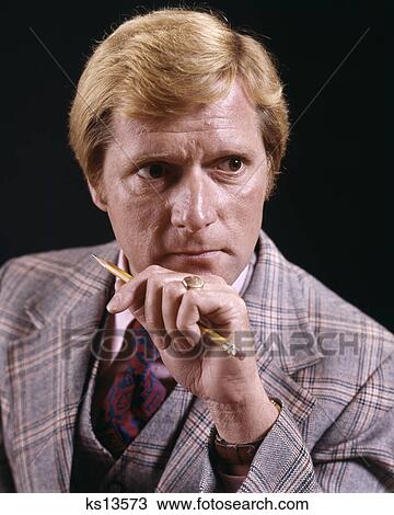 Stock Image - 1970s PORTRAIT MAN SERIOUS WORRIED CONCERNED EXPRESSION HOLDING PENCIL. Fotosearch