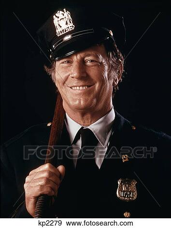 Stock Photo - 1970S Portrait Smiling Friendly Police Officer Looking At Camera Holding Nightstick. Fotosearch