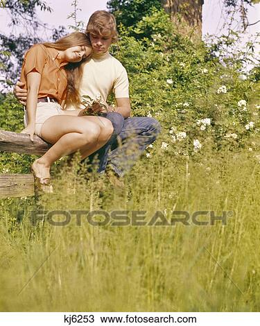 1970s ROMANTIC TEENAGE COUPLE SITTING ON WOODEN FENCE IN FIELD View Large Photo Image Stock Image - 1970s ROMANTIC TEENAGE COUPLE SITTING ON WOODEN FENCE IN FIELD. Fotosearch