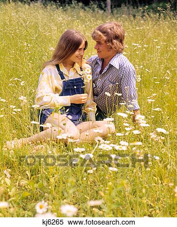 1970s ROMANTIC TEENAGE COUPLE SITTING IN A FIELD OF DAISIES View Large Photo Image Stock Photography - 1970s ROMANTIC TEENAGE COUPLE SITTING IN A FIELD OF DAISIES. Fotosearch