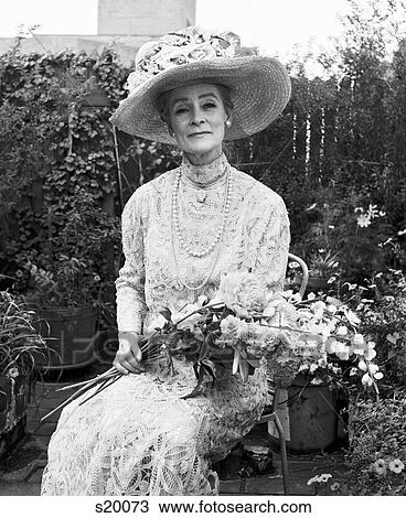 1970S Senior Woman Sitting In Garden Holding Bouquet Flowers Wearing Antique Lace Dress Big Hat Smiling Looking At Camera View Large Photo Image Stock Image - 1970S Senior Woman Sitting In Garden Holding Bouquet Flowers Wearing Antique Lace Dress Big Hat Smiling Looking At Camera. Fotosearch