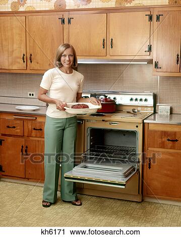 1970s SMILING BLOND WOMAN HOUSEWIFE LOOKING AT CAMERA HOLDING BAKED HAM STANDING BY STOVE OPEN OVEN DOOR View Large Photo Image Stock Image - 1970s SMILING BLOND WOMAN HOUSEWIFE LOOKING AT CAMERA HOLDING BAKED HAM STANDING BY STOVE OPEN OVEN DOOR. Fotosearch